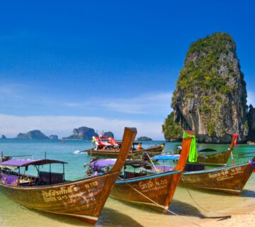 قارب تايلاندي تقليدي على شاطئ رملي مع صخور طبيعية ومياه صافية في جزر تايلاند